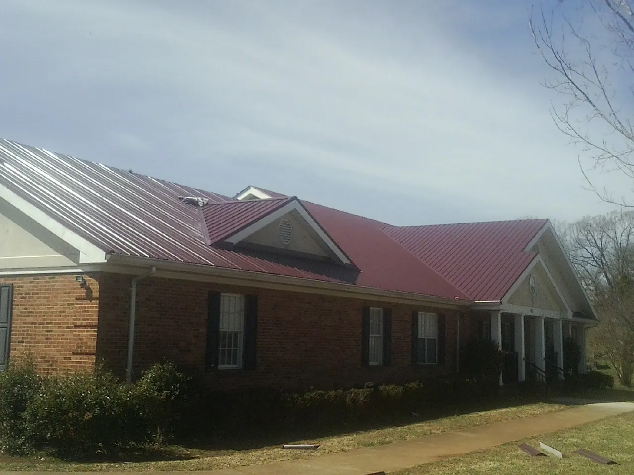 Red metal roof with gabled entries on a long brick building, from a Hail Damage Roof Repair job in Clarksdale
