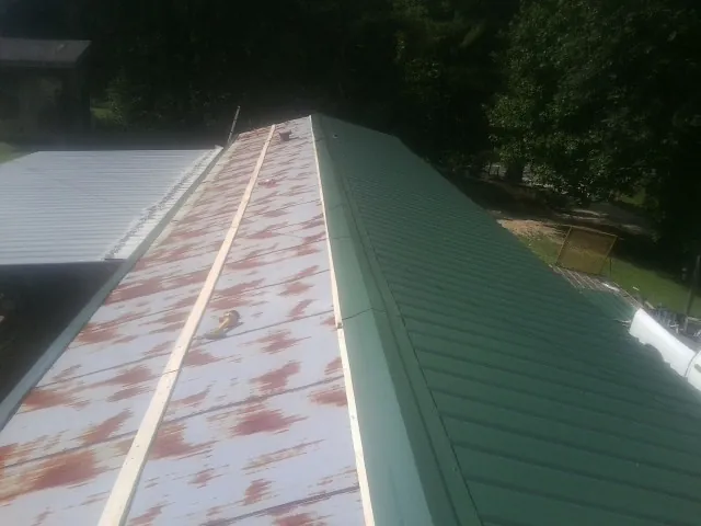 Old rusted panels beside newly installed green metal roofing — Wind Damage Roof Repair by Roofing Brothers in Clarksdale