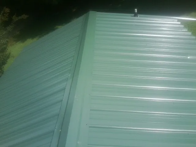 New green metal panels meeting at the ridge of a roof — Flat Roof Repair work by our crew in Clarksdale